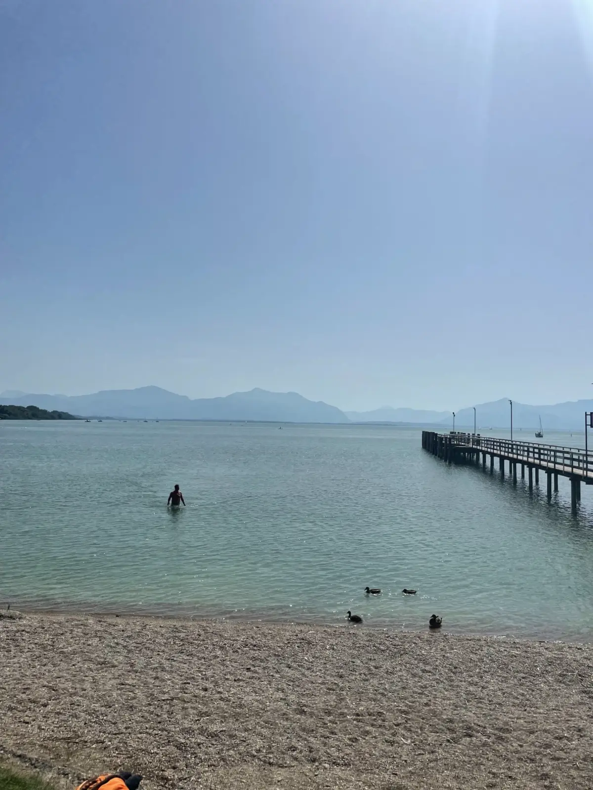 Badestopp am Chiemsee — türkisgrünes Wasser, der Steg und die Berge im Dunst.